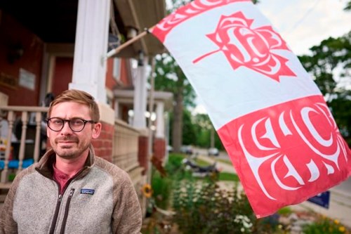 Blaine Chalk poses for a photo in front of his home in London, Ont., where he flies a version of the Canadian Flag designed by Indigenous artist Curtis Wilson, Monday, June 27, 2022. THE CANADIAN PRESS/Geoff Robins