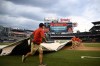 The scoreboard warns of inclement weather in the area as the Washington Nationals grounds crew rolls out the tarp on the field before a baseball game between the Nationals and the Seattle Mariners, Tuesday, July 12, 2022, in Washington. (AP Photo/Nick Wass)