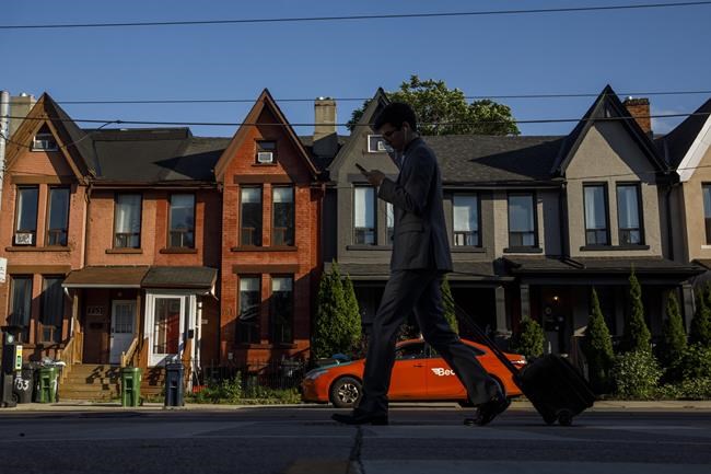 A person walks by a row of houses in Toronto on Tuesday July 12, 2022. Multigenerations living under one roof is becoming increasingly common, Statistics Canada's latest tranche of census data revealed Wednesday.THE CANADIAN PRESS/Cole Burston