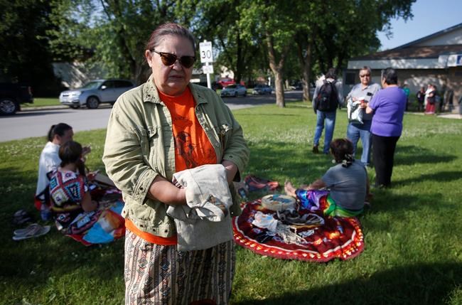 Victoria McIntosh, standing, holds a sweater she wore on her first day of school as supporters perform a ceremony and drum outside court in Powerview, Man., on Wednesday, July 20, 2022. McIntosh alleges 92-year-old priest Arthur Masse assaulted her when she was a student at a former residential school. THE CANADIAN PRESS/John Woods