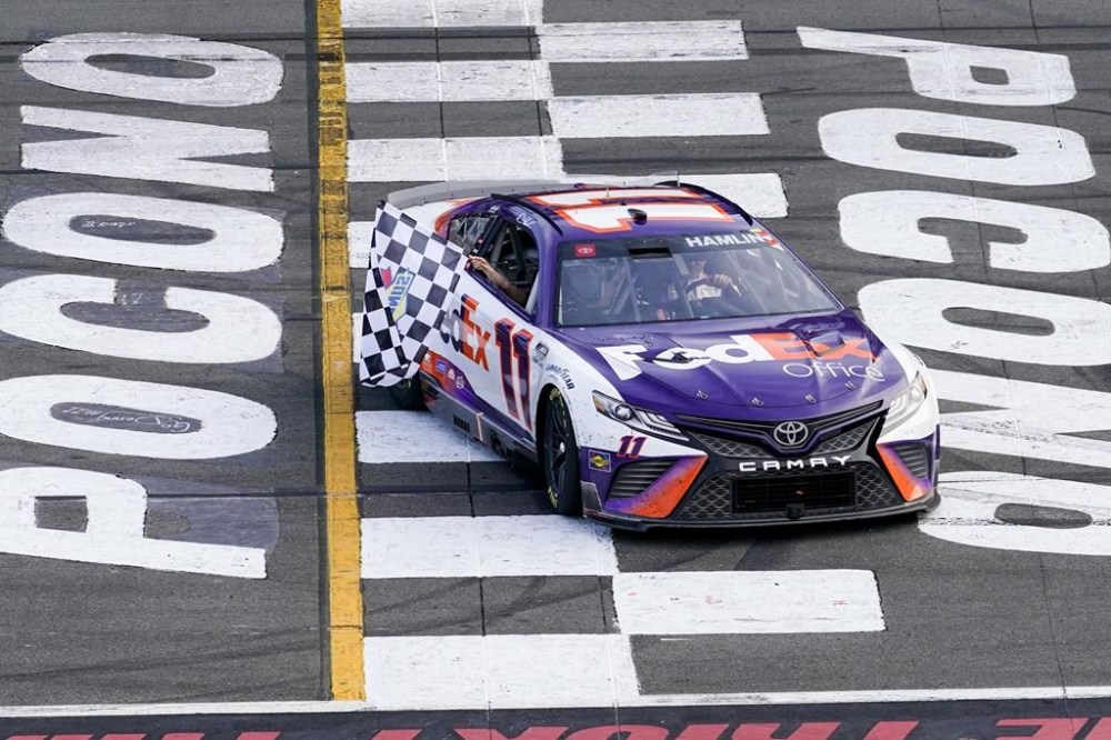 Taylor James Hamlin, left, waves the checker flag from inside the car with her dad, Denny Hamlin after he won the NASCAR Cup Series auto race at Pocono Raceway, Sunday, July 24, 2022, in Long Pond, Pa. (AP Photo/Matt Slocum)