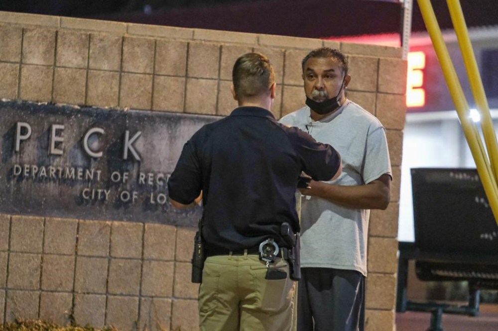 A police officer interviews a bystander near the scene of a shooting at Peck Park in San Pedro, Calif., Sunday, July 24, 2022. (AP Photo/Ringo H.W. Chiu)