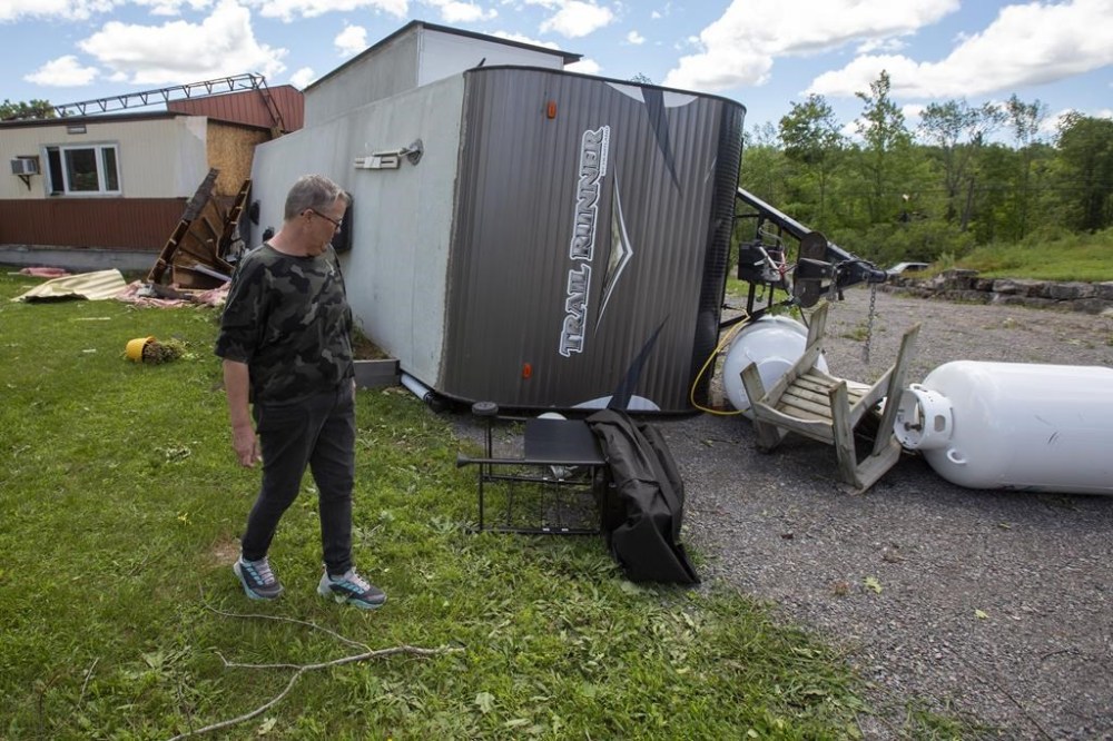 Lynn Prest walks beside her damaged house and overturned trailer from the aftermath of a possible tornado in Tweed, Ont., on Monday July 25, 2022. THE CANADIAN PRESS/Lars Hagberg