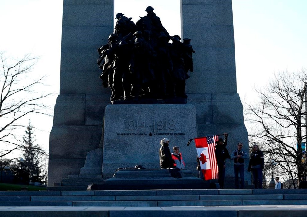 A person holds a combination American and Canadian flag at the Tomb of the Unknown Soldier at the National War Memorial before a march at a demonstration, part of a convoy-style protest participants are calling