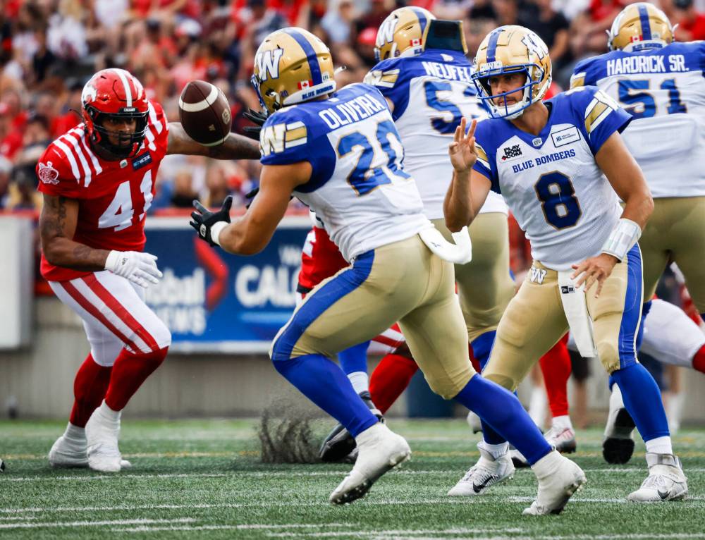 Winnipeg Blue Bombers quarterback Zach Collaros, right, tosses the ball to running back Brady Oliveira as Calgary Stampeders defensive lineman Mike Rose, left, looks on during the first half. (Jeff McIntosh / The Canadian Press)