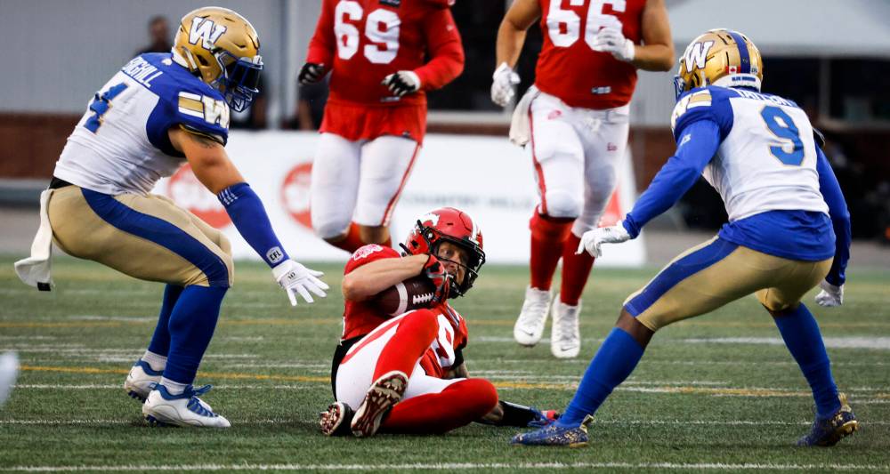 Winnipeg Blue Bombers linebacker Adam Bighill, left, and defensive back Nick Taylor, right, look on as Calgary Stampeders quarterback Bo Levi Mitchell slides for a first down during the second half. (Jeff McIntosh / The Canadian Press)