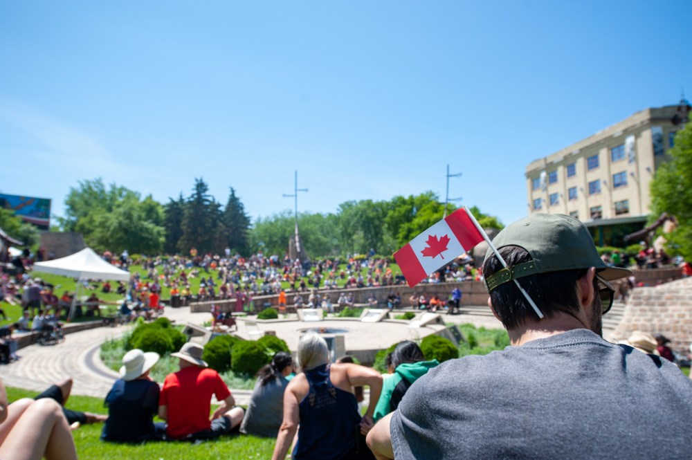 ETHAN CAIRNS / WINNIPEG FREE PRESS
A man sit with a flag in his hat at the A New Day Ceremony at The Forks Plaza in Winnipeg, Manitoba on Friday, July 1, 2022