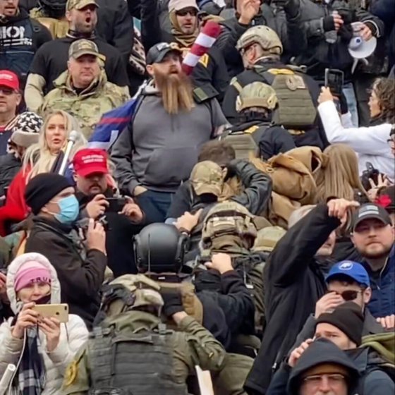 CPA line of men wearing helmets and body armour walk up the marble stairs outside the U.S. Capitol in Washington in an orderly single-file line, each man holding the jacket collar of the man ahead. (Robyn Stevens Brody / The Associated Press files)