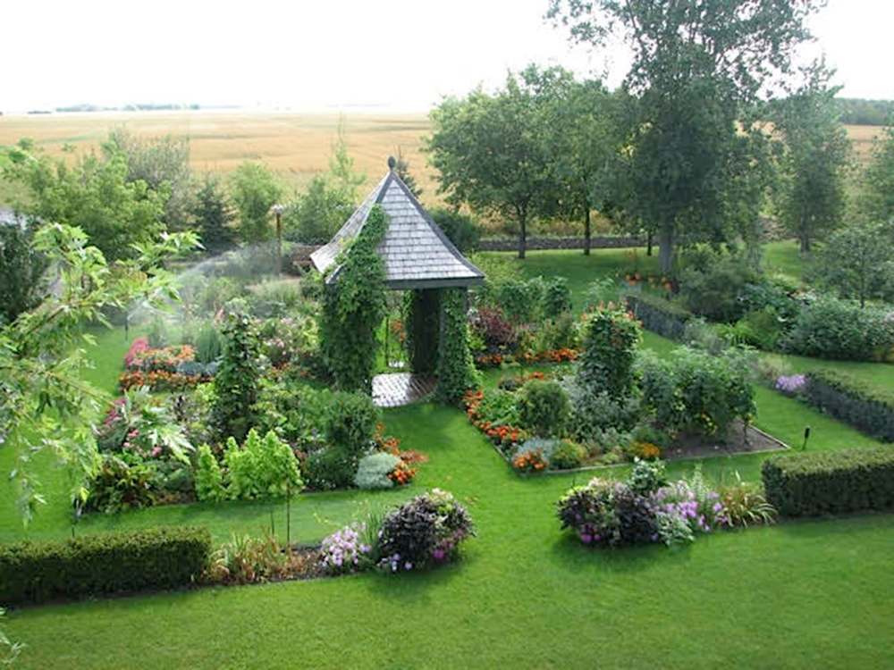 A garden house sits in the centre of a parterre-like garden planted with perennials and vegetables.