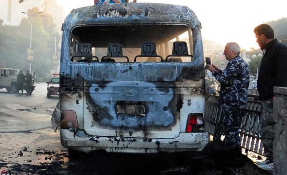 Syrian security officers beside the burned bus. (SANA via The Associated Press)