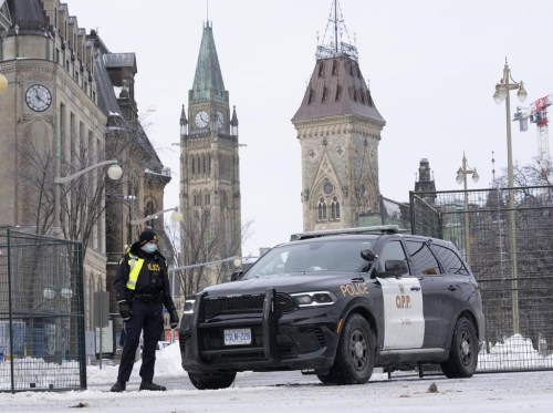A police officer stands at a checkpoint near Parliament Hill on Feb. 23, 2022 in Ottawa. The inquiry into Ottawa's unprecedented use of the Emergencies Act during protests in February is being delayed. The Public Order Emergency Commission announced today that it expects the hearings to start Oct. 13. It was originally supposed to start Sept. 19. THE CANADIAN PRESS/Adrian Wyld