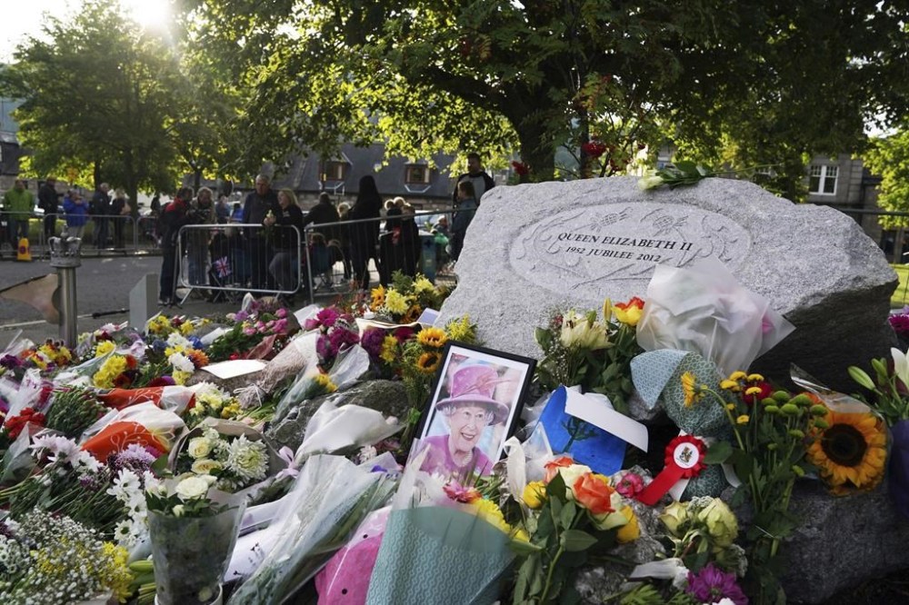 A photo of Queen Elizabeth II left among the flowers laid by members of the public at Balmoral, as the hearse carrying the coffin of Queen Elizabeth II, will travel to Edinburgh from Balmoral, Sunday Sept. 11, 2022. (Andrew Milligan/PA via AP)