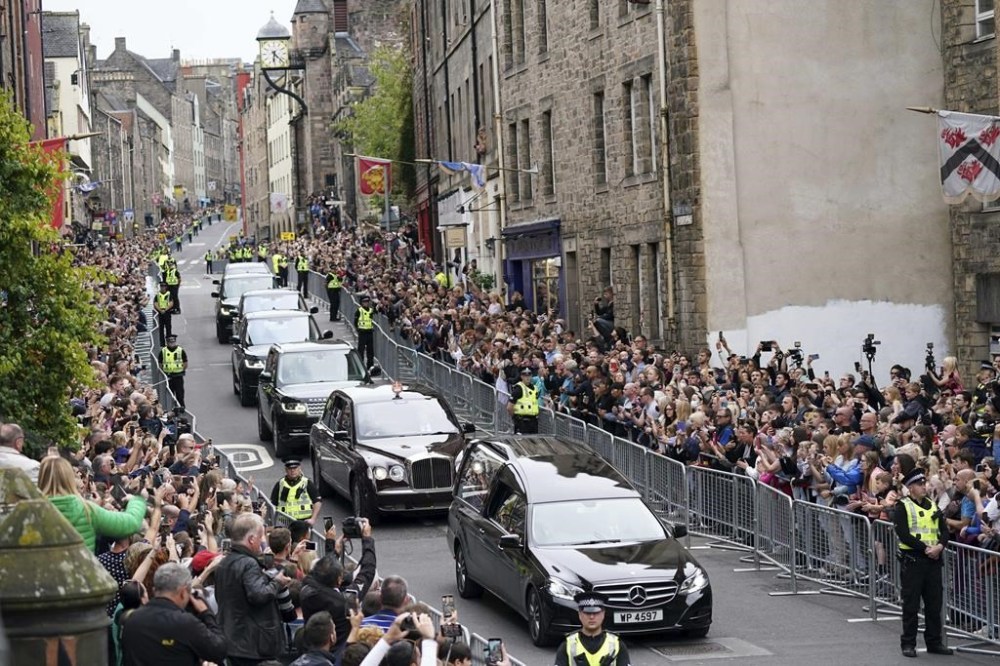 The hearse carrying the coffin of Queen Elizabeth II, draped with the Royal Standard of Scotland, passes along Canongate towards the Royal Mile as it completes its journey from Balmoral to the Palace of Holyroodhouse in Edinburgh, where it will lie in rest for a day, Sunday Sept. 11, 2022. (Jacob King/Pool Photo via AP)
