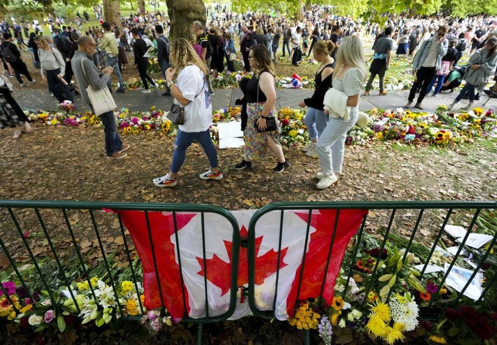 Long lines of mourners form and lay flowers near a Canadian flag as people wait to pay their respect near the gates of Buckingham Palace in London on Sunday, September 11, 2022. Queen Elizabeth II, Britain's longest-reigning monarch and a rock of stability across much of a turbulent century, died Thursday Sept. 8, 2022, after 70 years on the throne. She was 96. THE CANADIAN PRESS/Nathan Denette