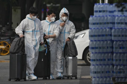 People wearing protective suits with their luggage enter the shuttered Communication University of China in Beijing, Monday, Sept. 12, 2022. Hundreds students at China's premier college for broadcast journalists have been sent to a quarantine center after a handful of COVID-19 cases were detected in their dormitory. (AP Photo/Andy Wong)