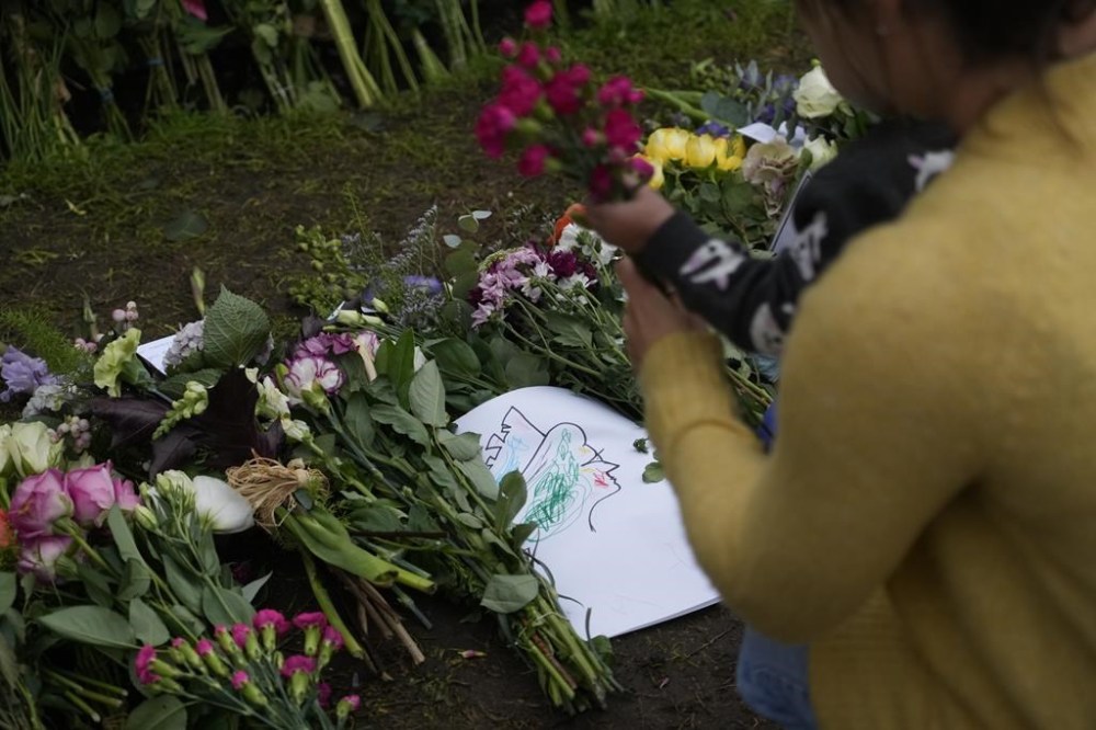 A mother with her baby lay flowers outside Windsor Castle for late Queen Elizabeth II in Windsor, England, Thursday, Sept. 15, 2022. The Queen will lie in state in Westminster Hall for four full days before her funeral on Monday Sept. 19. (AP Photo/Gregorio Borgia)