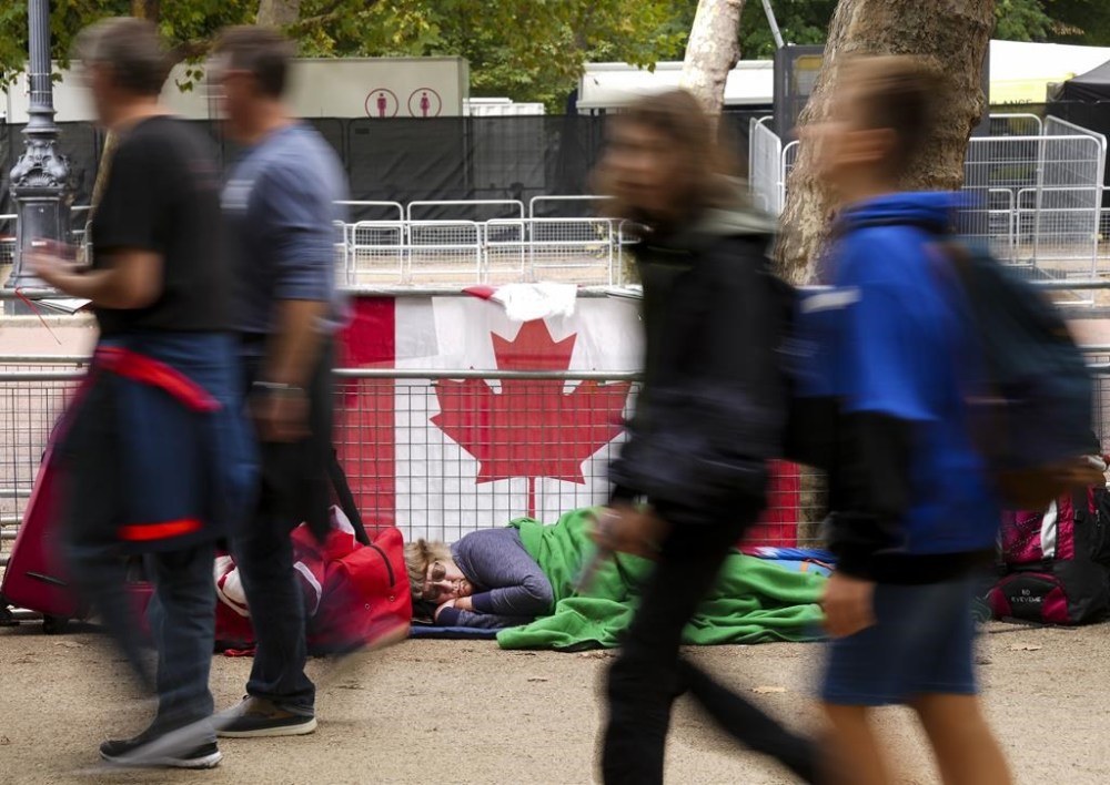 Bernadette Christie, of Grand Prairie, Alta., sleeps along a fence barricade as she and others camp out overnight in a tent to watch all the Queen's funeral ceremonies unfold near the gates of Buckingham Palace, in London, Thursday, Sept. 15, 2022. Queen Elizabeth II, Britain's longest-reigning monarch and a rock of stability across much of a turbulent century, died Thursday, Sept. 8, 2022, after 70 years on the throne. She was 96. THE CANADIAN PRESS/Nathan Denette