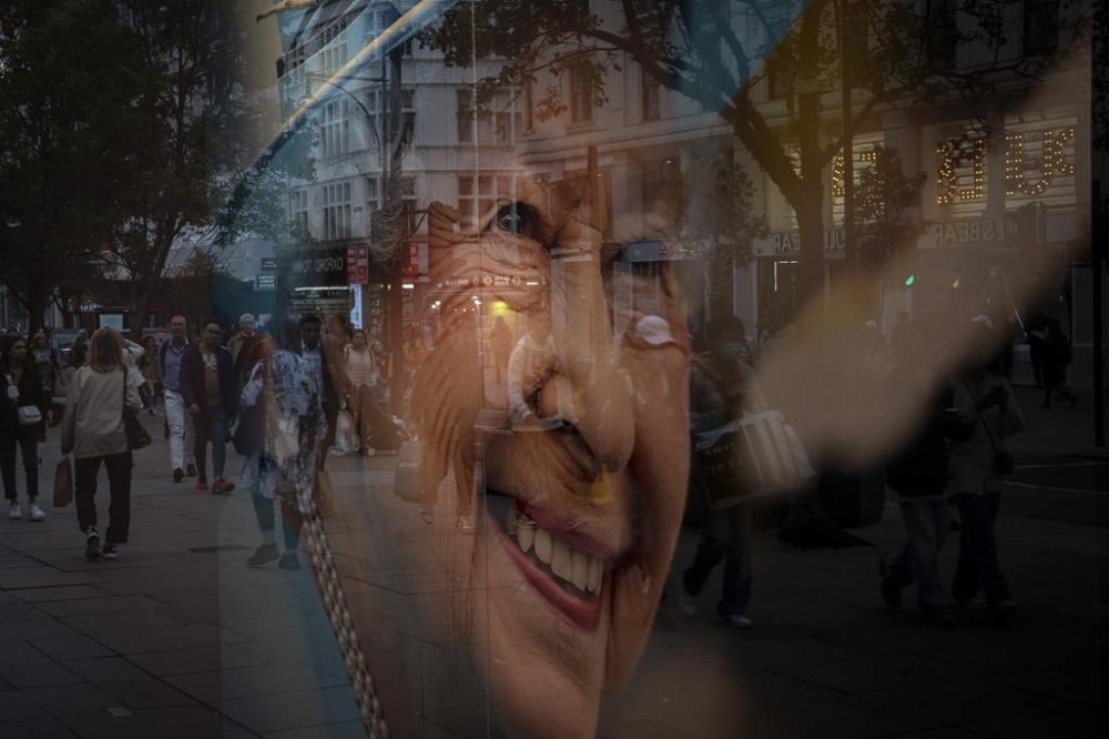 Pedestrians are seen reflected in the glass of a store displaying a portrait of the late Queen Elizabeth II in London, Thursday, Sept. 15, 2022. The Queen will lie in state in Westminster Hall for four full days before her funeral on Monday Sept. 19. (AP Photo/Emilio Morenatti)
