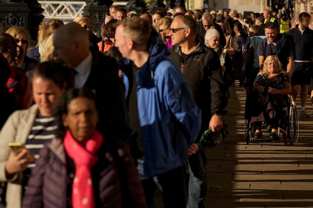 A wheelchair user is moved as people wait in line to pay their respects to late Queen Elizabeth II who is lying in state at Westminster Hall in London, Friday, Sept. 16, 2022. The Queen will lie in state in Westminster Hall for four full days before her funeral on Monday Sept. 19. (AP Photo/Andreea Alexandru)