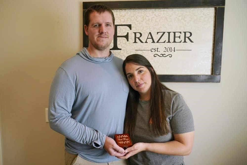 Adam and Abi Frazier hold the box containing the urn of their daughter Cadi Hope's ashes, Thursday, Aug. 18, 2022, in Mustang, Okla. Abi Frazier discovered at her 20-week anatomy scan that the baby she was carrying had a neural tube defect and other problems her doctors said were