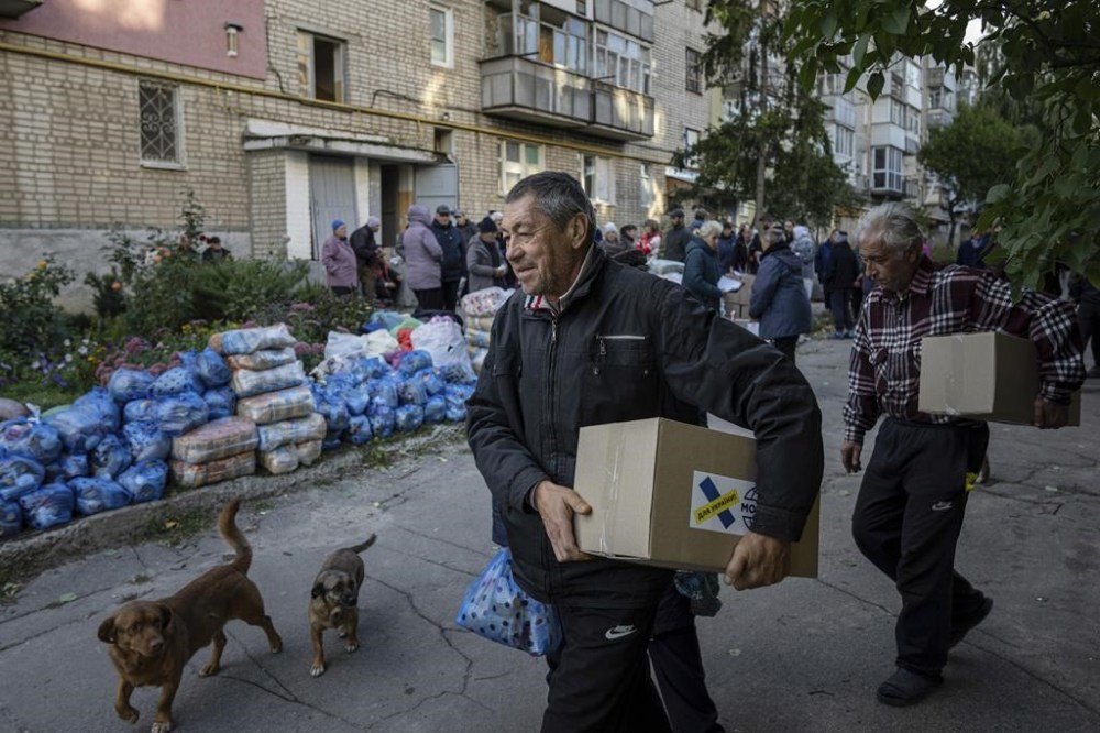 Men carry boxes with humanitarian aid at the distribution point in the recently retaken town of Izium, Ukraine, Sunday, Sept. 25, 2022. (AP Photo/Evgeniy Maloletka)