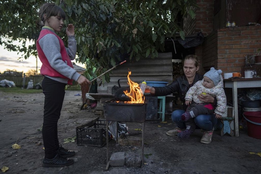 Margaryta Tkachenko, 29, warms food on an open fire for her 9-month-old daughter Sophia in the recently retaken town of Izium, Ukraine, Sunday, Sept. 25, 2022. (AP Photo/Evgeniy Maloletka)