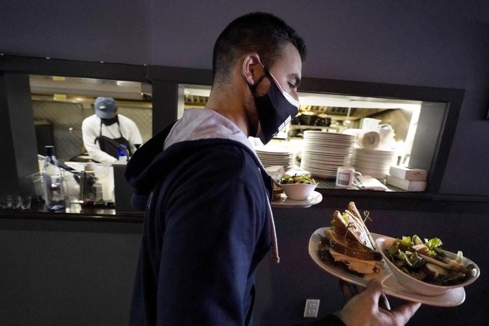 FILE - Bartender Denis Angelov carries plates of food from the kitchen, behind, at Tin Pan Alley restaurant, Tuesday, April 6, 2021, in Provincetown, Mass. The number of available jobs in the U.S. plummeted in August 2022 compared with July as businesses grow less desperate for workers, a trend that could cool chronically high inflation.  (AP Photo/Steven Senne, File)