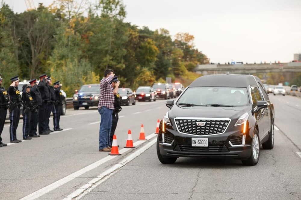 A private funeral for two Ontario police officers killed in a shooting in Innisfil last week will be held in Barrie today. Const. Morgan Russell, 54, and Const. Devon Northrup, 33, died after responding to a call in Innisfil on Oct. 11, 2022. Ontario Provincial Police officer Adam McCourt, left in plainclothes, and Sgt. Jonathan Bouchard salute the arriving procession carrying the bodies of the two officers on Friday, Oct. 14, 2022. THE CANADIAN PRESS/Christopher Drost