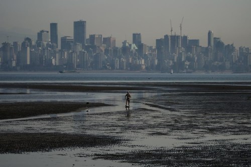A man jumps on a skimboard while riding on tidal pools at Spanish Banks as smoke from wildfires hangs over the downtown core, in Vancouver, B.C., Thursday, Oct. 6, 2022. A group of doctors says Canada's health-care system is not prepared for the worsening effects of climate change and failing to adapt would mean more lives lost. THE CANADIAN PRESS/Darryl Dyck