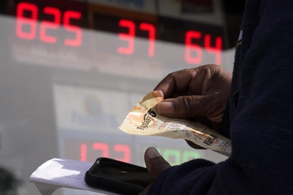 A customer holds a lottery ticket as she waits in line at Bluebird Liquor, Friday, Oct. 28, 2022, in Hawthorne, Calif. Saturday's jackpot projected winnings of an estimated $825 million is the fifth-highest in U.S. history. (AP Photo/Mark J. Terrill)