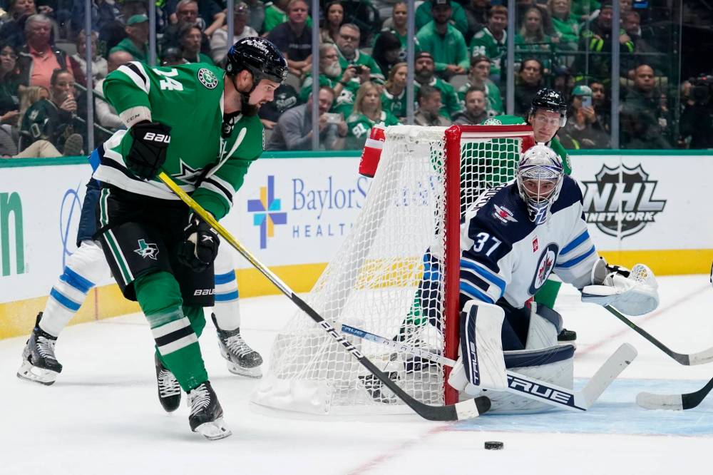 Jamie Benn makes a pass to the front of the net as Winnipeg Jets goaltender Connor Hellebuyck holds the post in the first period on Monday. (Tony Gutierrez / The Associated Press)