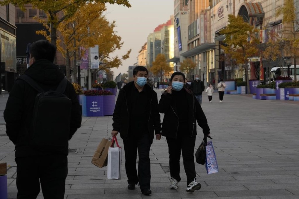 Residents wearing masks carry bags as they visit the Wangfujing shopping street in Beijing, Monday, Nov. 14, 2022. Chinese consumer spending contracted in October and factory activity weakened as anti-virus controls following a rise in infections weighed on the economy. (AP Photo/Ng Han Guan)