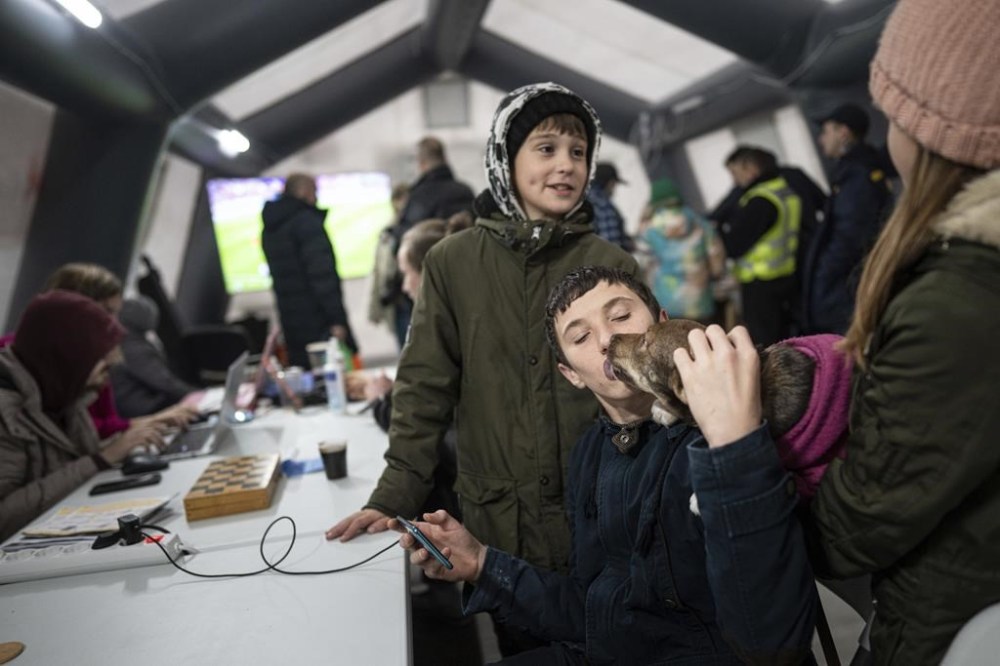 A boy kisses a dog while he charges his phone at the heating tent