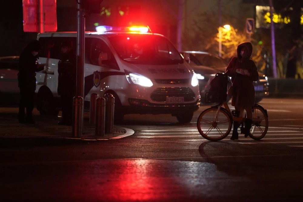 A passerby on a bicycle stops near a police van monitoring an area where protesters were expected to gather in Beijing, Monday, Nov. 28, 2022. Chinese authorities eased some anti-virus rules but affirmed their severe