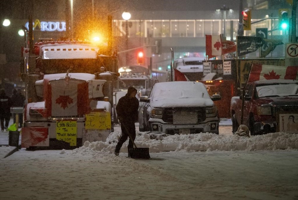 A protester shovels snow in front of parked semi-trailer and pickup trucks on Rideau Street, on the 21st day of a protest against COVID-19 measures that has grown into a broader anti-government protest, in Ottawa, on Thursday, Feb. 17, 2022. The Defence Department's top official says he told the military to prepare to intervene as