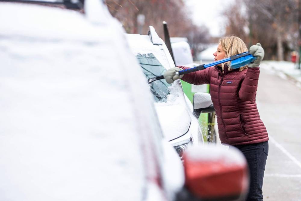 Alison August scrapes her car off Monday during one of the first snowy mornings of the season. (Mikaela MacKenzie / Winnipeg Free Press)