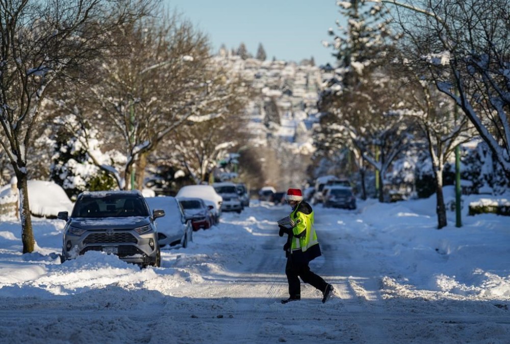 A Canada Post letter carrier crosses a snowy and ice-covered road while delivering mail in Burnaby, B.C., on Wednesday, Dec 21, 2022. A snowstorm dumped more than 30 centimetres of snow in Metro Vancouver this week. THE CANADIAN PRESS/Darryl Dyck