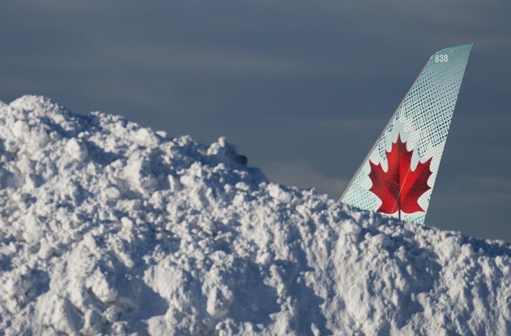 The tail of an Air Canada aircraft is seen behind a pile of snow at Vancouver International Airport in Richmond, B.C., Wednesday, Dec. 21, 2022. The airport is limiting international flights to carriers registered in Canada and the U.S. for two days as it attempts to clear a backlog of aircraft and passengers after a snowstorm caused massive disruptions this week. THE CANADIAN PRESS/Darryl Dyck