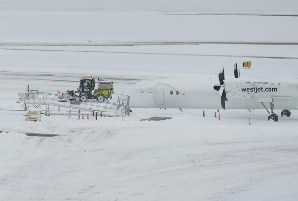 A worker clears snow on the apron near a WestJet aircraft at Vancouver International Airport after a snowstorm crippled operations leading to cancellations and major delays, in Richmond, B.C., on Tuesday, Dec. 20, 2022. THE CANADIAN PRESS/Darryl Dyck