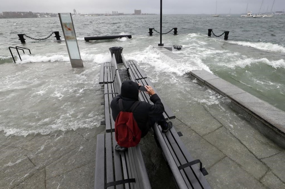 Brooks Payne photographs flood waters during high tide on Long Wharf, Friday, Dec. 23, 2022, in Boston. Winter weather is blanketing the U.S. More than 200 million people — about 60% of the U.S. population — were under some form of winter weather advisory or warning on Friday. (AP Photo/Michael Dwyer)