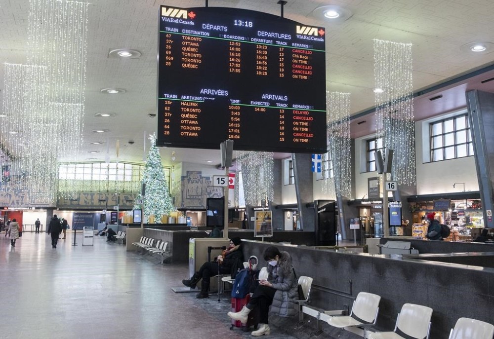 People sit near a Via Rail schedule board at central station in Montreal Monday, December 26, 2022. A Christmas Eve train derailment is also continuing to wreak havoc on holiday travel plans in Ontario and Quebec. THE CANADIAN PRESS/Graham Hughes