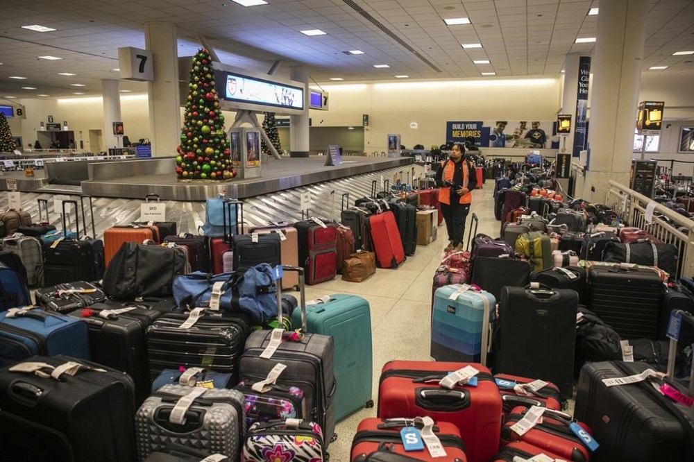 Airport staff walks around a pile of lost suitcases near the baggage carousel at Midway Airport in Chicago, Tuesday, Dec. 27, 2022, after Southwest Airlines flights were cancelled and delayed during a winter storm. Problems at Southwest Airlines appeared to snowball after the worst of the storm passed. It cancelled more than 70% of its flights Monday, more than 60% on Tuesday, and warned that it would operate just over a third of its usual schedule in the days ahead to allow crews to get back to where they needed to be. (Pat Nabong /Chicago Sun-Times via AP)