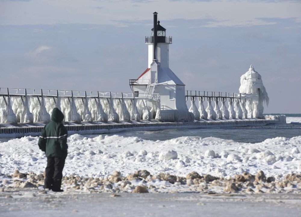 A man views the ice covered St. Joseph Lighthouses, from the safety of Tiscornia Beach Tuesday, Dec. 27, 2022, in St. Joseph, Mich.(Don Campbell /The Herald-Palladium via AP)