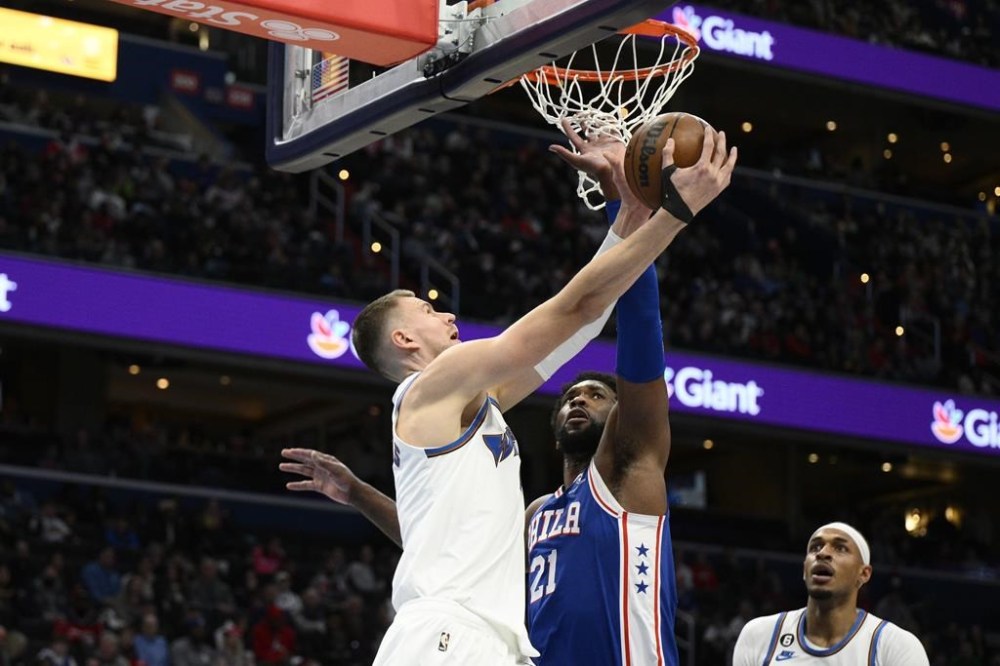 Washington Wizards center Kristaps Porzingis, left, goes to the basket against Philadelphia 76ers center Joel Embiid (21) during the first half of an NBA basketball game, Tuesday, Dec. 27, 2022, in Washington. (AP Photo/Nick Wass)