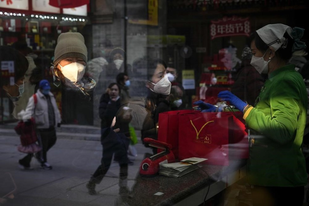 People are reflected on a window panel as visitors wearing face masks buy tea products in Qianmen, a popular tourist spot in Beijing, Tuesday, Jan. 3, 2023. As the virus continues to rip through China, global organizations and governments have called on the country start sharing data while others have criticized its current numbers as meaningless. (AP Photo/Andy Wong)