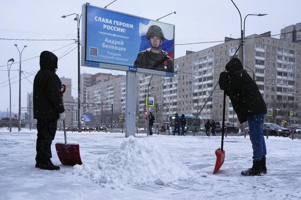 Workers clear the snow next to a billboard with a portrait of a Russian soldier awarded for action in Ukraine and the words