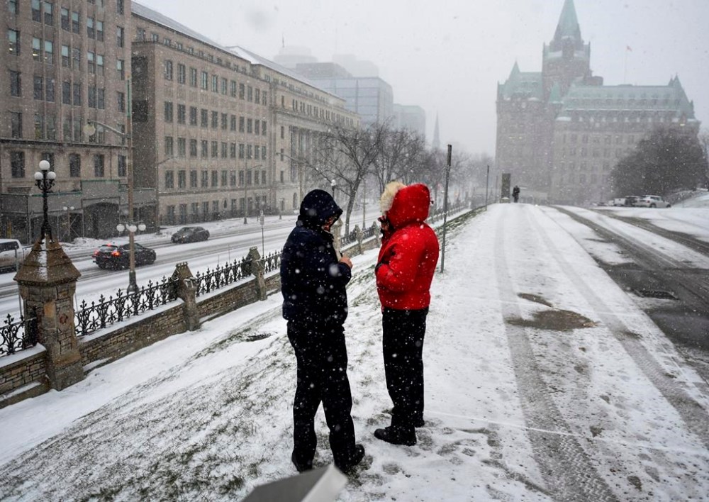 People keep warm in their winter coats as they vape outside Parliament Hill’s West Block as snow falls in Ottawa, on Wednesday, Dec. 15, 2021. Advocates on both sides of the vaping debate say the government must do more to enforce penalties for selling vapes to kids after a review concluded no changes to the legislation were warranted. THE CANADIAN PRESS/Justin Tang