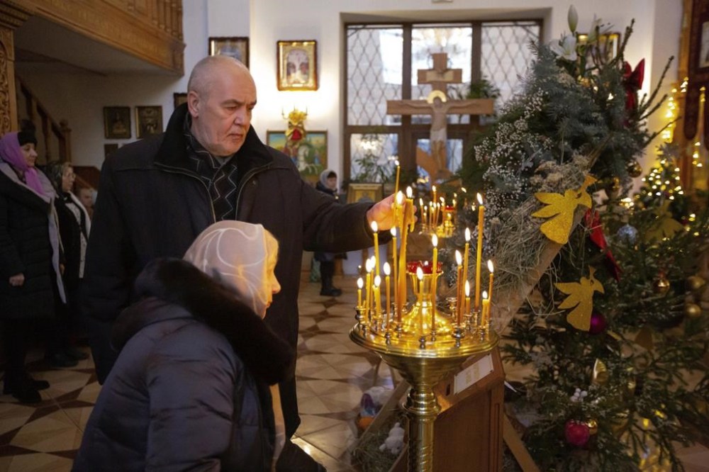 A man lights a candle as other parishioners attend the Christmas service in an Orthodox church in Dometsk, Russian-controlled Donetsk region, eastern Ukraine, Saturday, Jan. 7, 2023. Orthodox Christians celebrate Christmas on Jan. 7, in accordance with the Julian calendar. (AP Photo/Alexei Alexandrov)