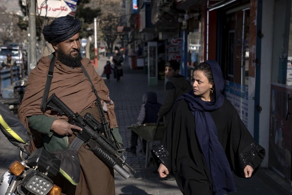 A Taliban fighter stands guard as a woman walks past in Kabul, Afghanistan, on Dec. 26, 2022. An all-party group of MPs is calling on the Canadian government to help former female lawmakers in Afghanistan reach safety. Police in Kabul said Sunday that former MP Mursal Nabizada and her bodyguard were shot dead by unknown attackers. THE CANADIAN PRESS/AP-Ebrahim Noroozi
