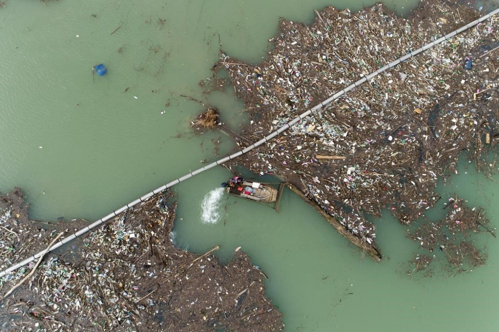 Utility company workers push the waste to the shore of Lim river near Priboj, Serbia, Monday, Jan. 30, 2023. Plastic bottles, wooden planks, rusty barrels and other garbage dumped in poorly regulated riverside landfills or directly into the rivers accumulated during high water season, behind a trash barrier in the Lim river in southwestern Serbia. (AP Photo/Armin Durgut)